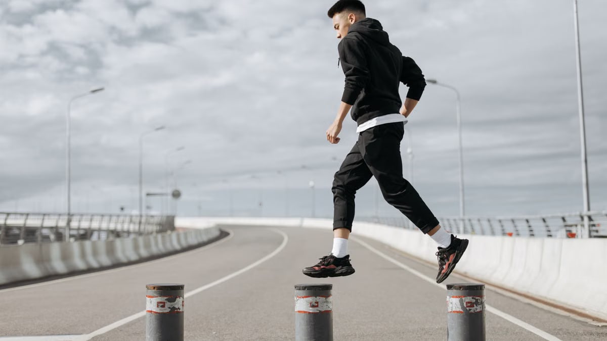 A young man is exercising by leaping over road barriers on a modern city street.